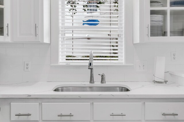 kitchen featuring white cabinets, decorative backsplash, light stone countertops, and sink