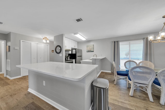 kitchen with stainless steel appliances, white cabinetry, pendant lighting, light wood-type flooring, and a chandelier