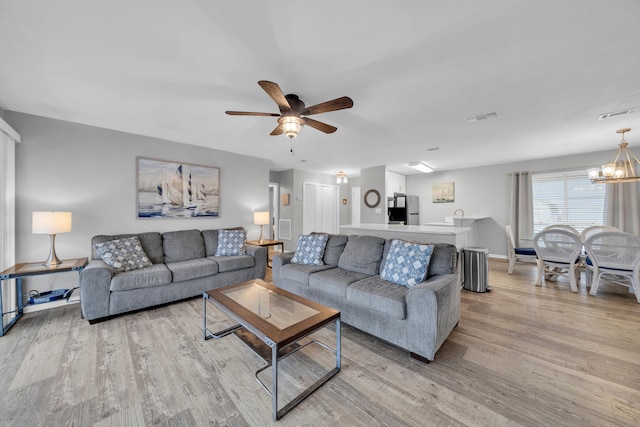 living room with ceiling fan with notable chandelier and light hardwood / wood-style floors