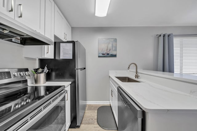 kitchen featuring light stone countertops, white cabinetry, appliances with stainless steel finishes, sink, and light hardwood / wood-style floors