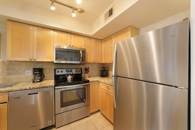 kitchen featuring light brown cabinets, light stone countertops, stainless steel appliances, tasteful backsplash, and rail lighting