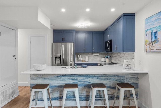 kitchen with blue cabinets, sink, a breakfast bar area, stainless steel appliances, and light hardwood / wood-style flooring