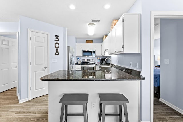 kitchen featuring kitchen peninsula, appliances with stainless steel finishes, hardwood / wood-style flooring, white cabinetry, and sink