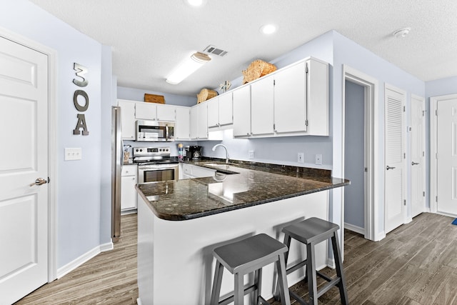 kitchen featuring kitchen peninsula, appliances with stainless steel finishes, sink, hardwood / wood-style flooring, and a textured ceiling