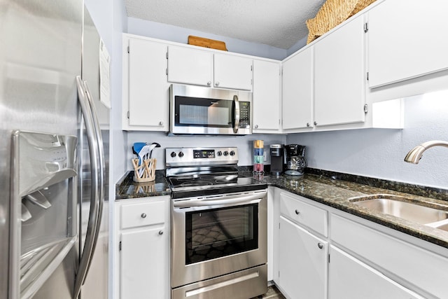 kitchen featuring appliances with stainless steel finishes, dark stone countertops, white cabinets, and a textured ceiling