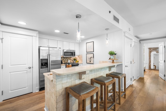 kitchen with appliances with stainless steel finishes, light hardwood / wood-style flooring, decorative backsplash, a breakfast bar area, and white cabinets