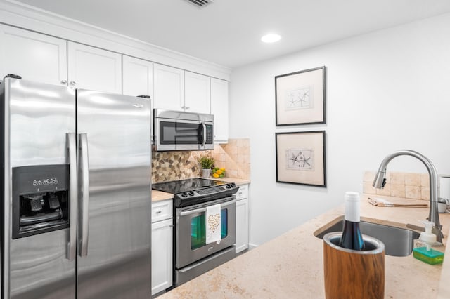 kitchen with appliances with stainless steel finishes, white cabinetry, tasteful backsplash, sink, and light stone counters