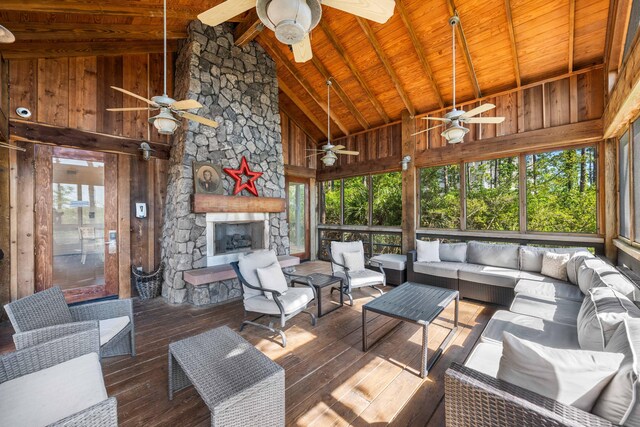 sunroom / solarium featuring wood ceiling, ceiling fan, vaulted ceiling with beams, and a stone fireplace