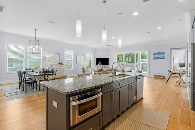 kitchen with sink, appliances with stainless steel finishes, light hardwood / wood-style flooring, and a kitchen island with sink