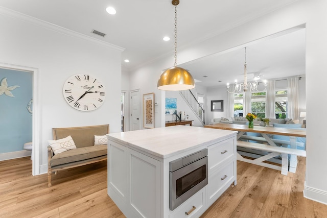 kitchen with a kitchen island, white cabinetry, stainless steel microwave, decorative light fixtures, and light hardwood / wood-style flooring