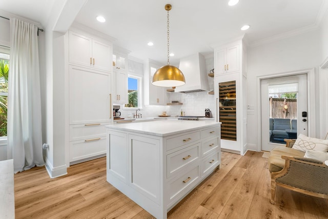 kitchen with a kitchen island, custom exhaust hood, white cabinets, and light wood-type flooring