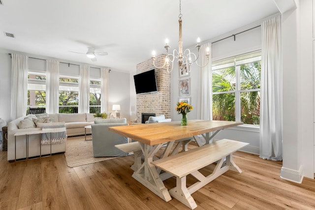 dining space featuring ceiling fan with notable chandelier, light hardwood / wood-style floors, and a brick fireplace