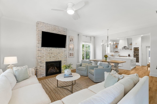 living room with brick wall, ceiling fan with notable chandelier, light wood-type flooring, and a fireplace