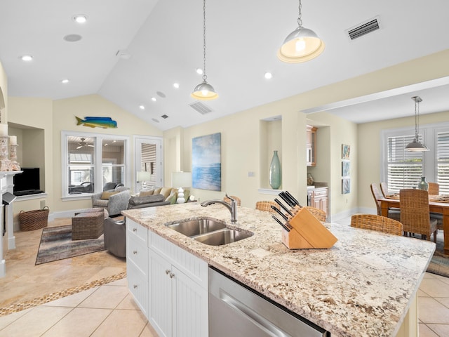 kitchen with stainless steel dishwasher, sink, light tile floors, and a kitchen island with sink