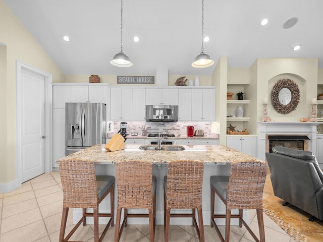 kitchen with white cabinetry, stainless steel appliances, light tile floors, a center island with sink, and tasteful backsplash