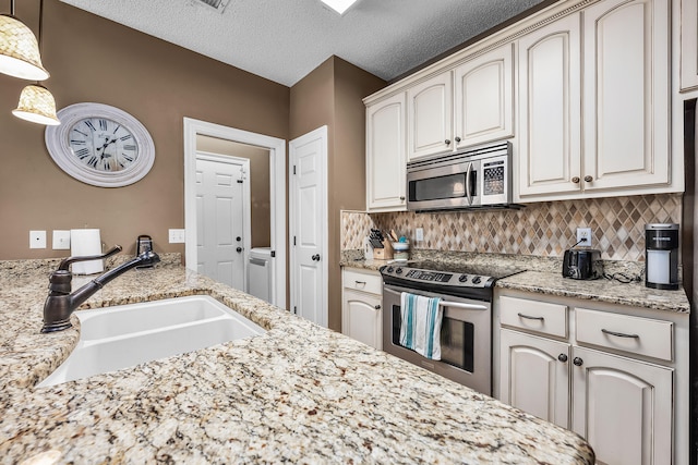 kitchen featuring a textured ceiling, hanging light fixtures, appliances with stainless steel finishes, backsplash, and sink