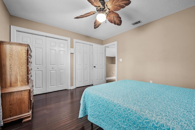 bedroom with multiple closets, a textured ceiling, ceiling fan, and dark hardwood / wood-style floors