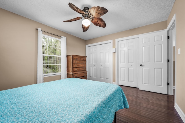 bedroom with dark hardwood / wood-style flooring, two closets, ceiling fan, and a textured ceiling