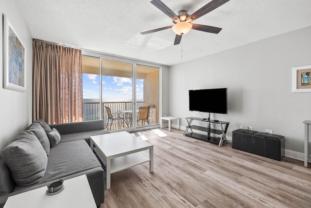 living room featuring light hardwood / wood-style flooring, ceiling fan, expansive windows, and a textured ceiling