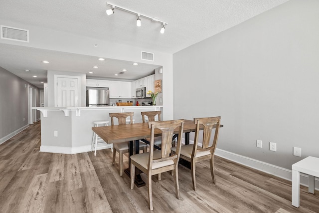 dining room with rail lighting, a textured ceiling, and light wood-type flooring