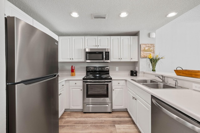 kitchen featuring a textured ceiling, white cabinets, sink, light hardwood / wood-style floors, and stainless steel appliances