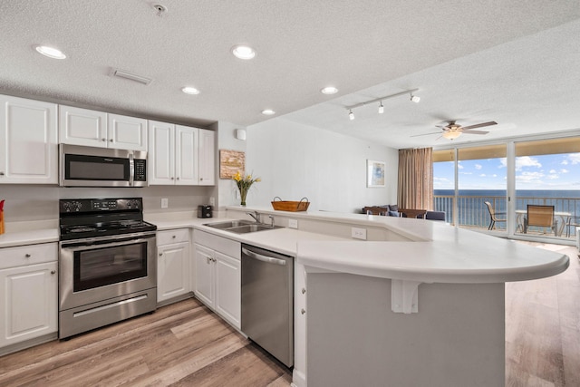 kitchen with light hardwood / wood-style flooring, rail lighting, kitchen peninsula, stainless steel appliances, and a textured ceiling