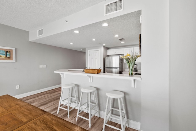 kitchen featuring a textured ceiling, white cabinets, light hardwood / wood-style floors, stainless steel refrigerator, and a kitchen breakfast bar