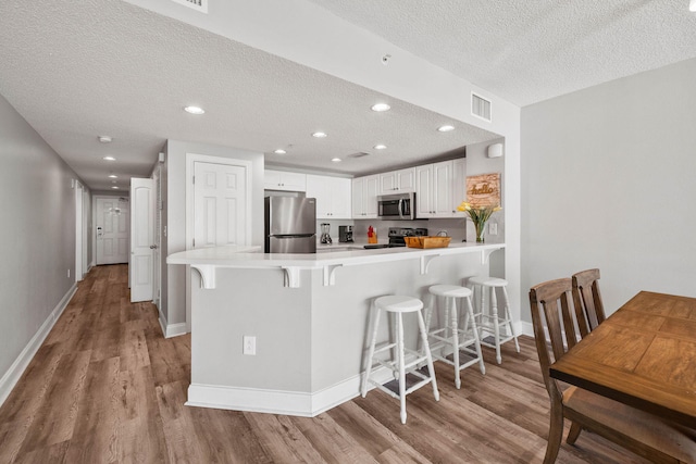 kitchen with stainless steel appliances, white cabinets, a breakfast bar area, and light wood-type flooring