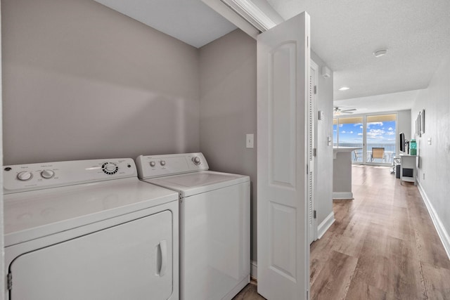 washroom featuring light hardwood / wood-style flooring, ceiling fan, washing machine and dryer, and a textured ceiling