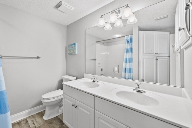 bathroom with large vanity, toilet, a textured ceiling, double sink, and hardwood / wood-style floors