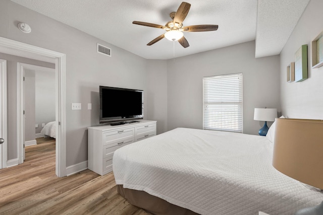 bedroom featuring light hardwood / wood-style floors, ceiling fan, and a textured ceiling