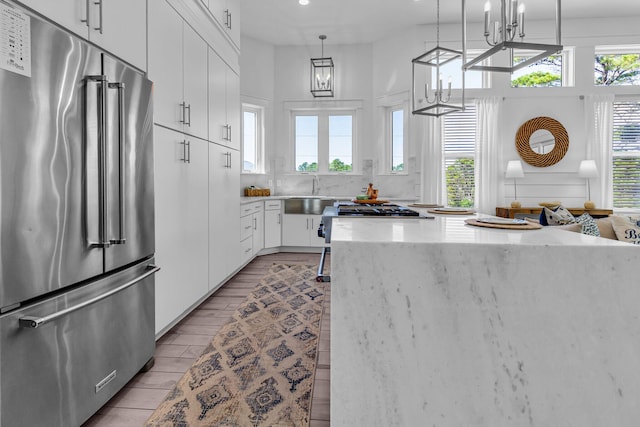 kitchen with a healthy amount of sunlight, hanging light fixtures, white cabinets, light wood-type flooring, and high end fridge