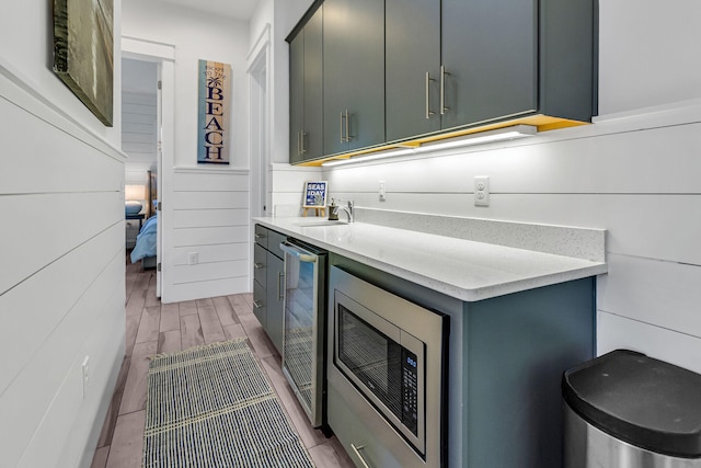 kitchen featuring wine cooler, hardwood / wood-style floors, stainless steel microwave, sink, and light stone counters