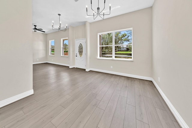 empty room with ceiling fan with notable chandelier, plenty of natural light, and hardwood / wood-style flooring