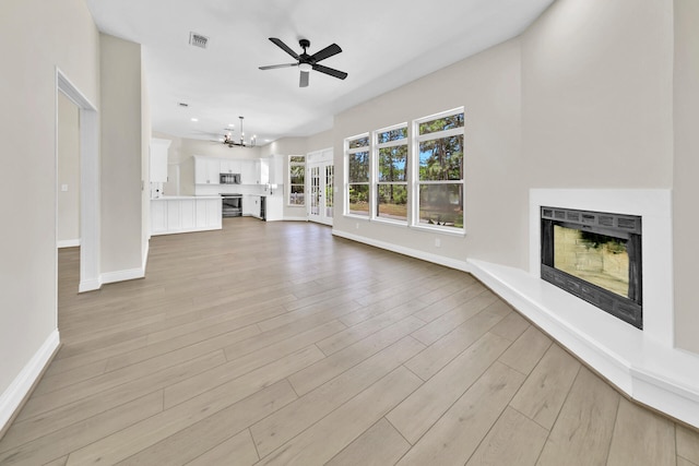 unfurnished living room featuring ceiling fan with notable chandelier and light hardwood / wood-style floors