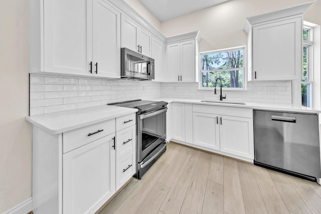 kitchen featuring appliances with stainless steel finishes, tasteful backsplash, white cabinets, sink, and light wood-type flooring