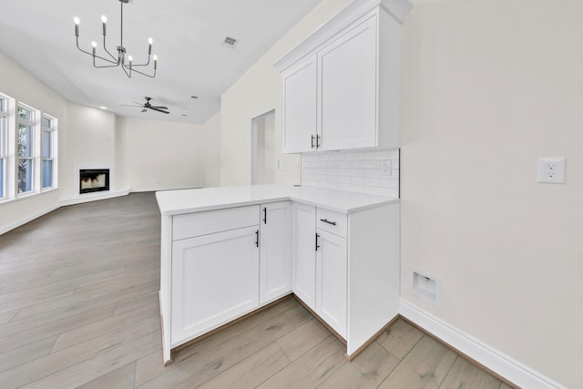 kitchen with ceiling fan with notable chandelier, kitchen peninsula, and light wood-type flooring