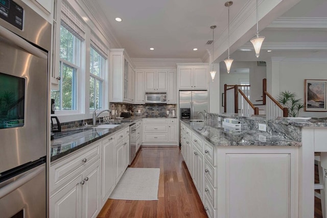 kitchen with hanging light fixtures, stainless steel appliances, wood-type flooring, an island with sink, and white cabinetry