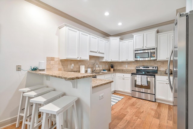 kitchen with kitchen peninsula, appliances with stainless steel finishes, light hardwood / wood-style flooring, light stone counters, and white cabinets