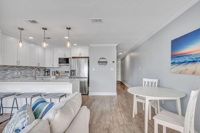 kitchen with crown molding, white cabinetry, hanging light fixtures, and stainless steel appliances