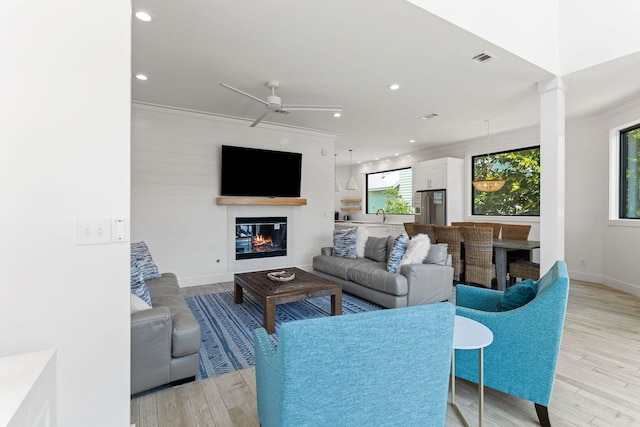 living area with light wood finished floors, visible vents, a glass covered fireplace, ceiling fan, and recessed lighting