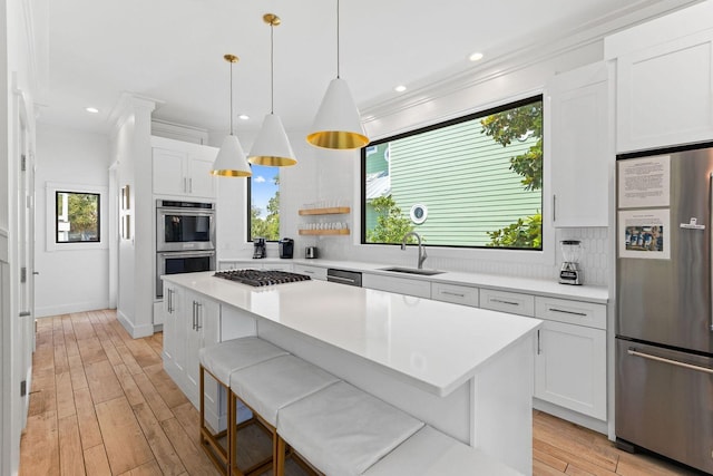 kitchen with crown molding, light wood finished floors, stainless steel appliances, white cabinetry, and a kitchen island