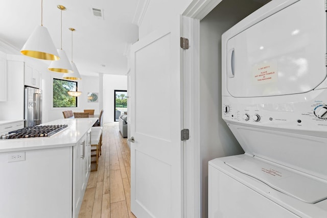 clothes washing area with laundry area, visible vents, light wood-style floors, stacked washer / drying machine, and ornamental molding