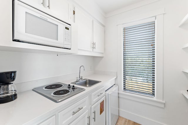 kitchen with white microwave, stainless steel electric stovetop, a sink, white cabinetry, and light countertops