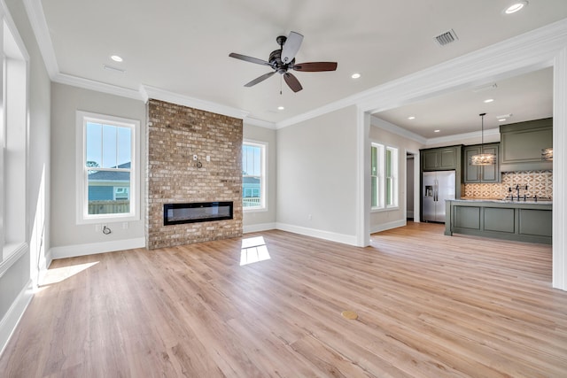 unfurnished living room with ceiling fan, sink, light hardwood / wood-style flooring, crown molding, and a fireplace