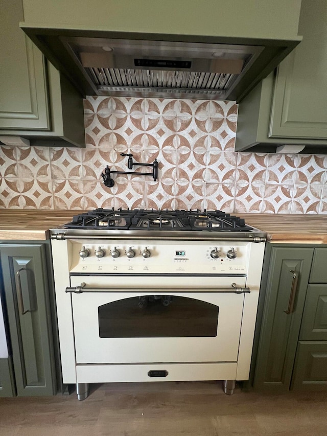 kitchen featuring green cabinets, wall chimney exhaust hood, tasteful backsplash, butcher block countertops, and gas range gas stove