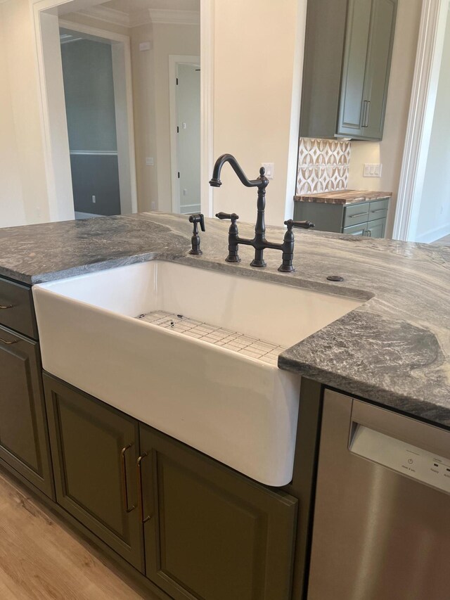 kitchen featuring light wood-type flooring, tasteful backsplash, stainless steel dishwasher, dark stone counters, and sink