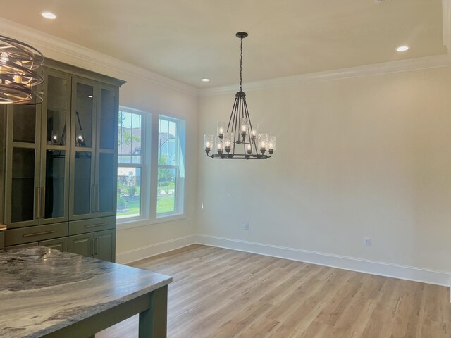 unfurnished dining area featuring an inviting chandelier, ornamental molding, and light hardwood / wood-style flooring