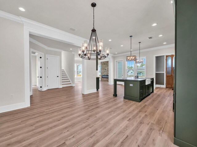 kitchen featuring a center island with sink, crown molding, hanging light fixtures, light wood-type flooring, and a chandelier