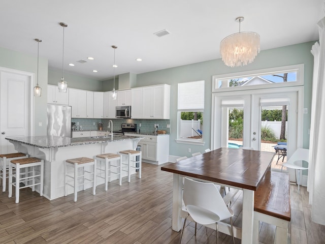 dining space featuring sink, french doors, light wood-type flooring, and an inviting chandelier